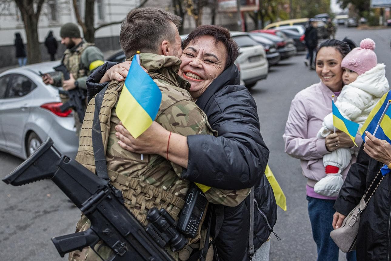 A smiling woman joyfully embraces a Ukrainian soldier in camouflage gear on the street.